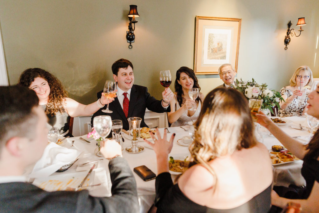 A wedding couple toasting wine glasses with guests seated around them