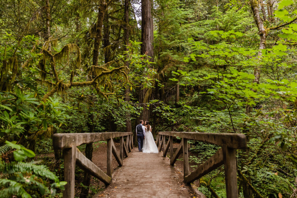 A couple walks along a forested wooden bridge during their redwoods elopement.
